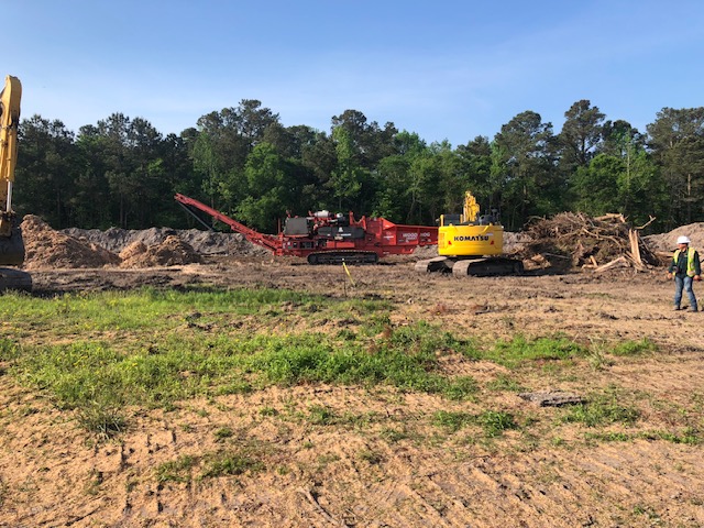 Horizontal grinder and Komatsu excavator processing land-clearing debris