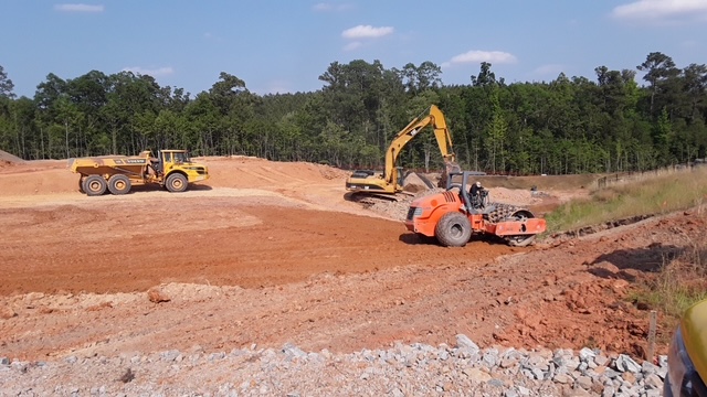 Articulated haul truck, excavator, and padfoot roller building embankment